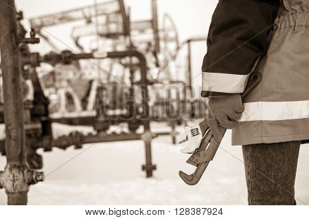 Working hand with wrenches on a wellhead crude oil site background. Toned sepia.