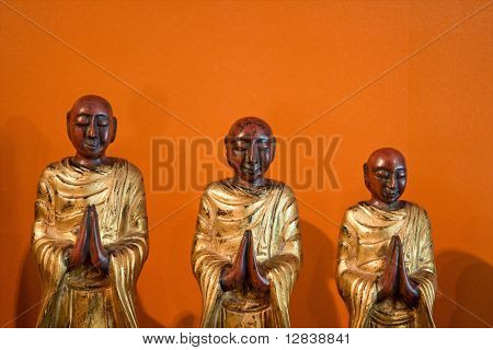 Három fa szobrok buddhista tanítványok narancssárga falnak.