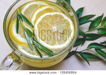 Glass cup of ginger tea with yellow lemon served round frame green leaves ruscus flowers on a light wooden rustic wall background. Still life food and drink healthcare concept top view. Eco style. With spase for text.