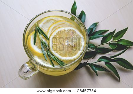 Glass cup of ginger tea with lemon, rosemary served round frame green leaves ruscus flowers on a light wooden rustic wall background. Still life, organic drink and food, healthcare concept, top view. Eco style. Health concept.
