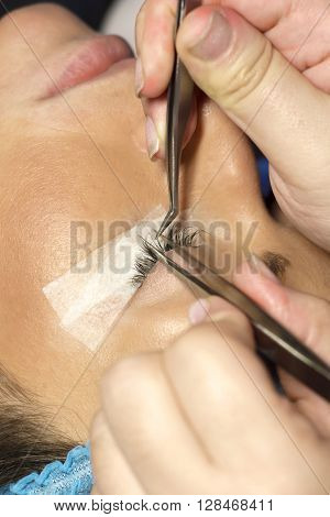 Eyelash extension procedure in beauty salon. Tweezers in hands of tehnician