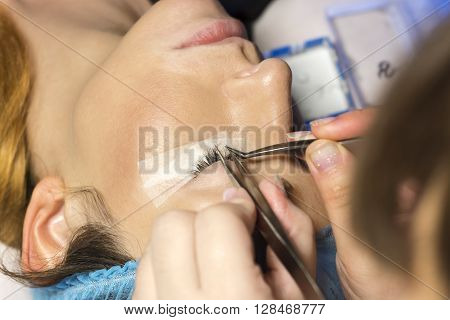 Eyelash extension procedure in beauty salon. Tweezers in hands of tehnician