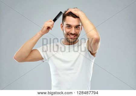beauty, grooming and people concept - smiling young man brushing hair with comb over gray background