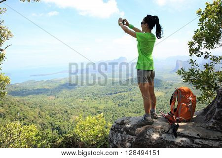 young woman hiker use smartphone taking photo on seaside mountain top
