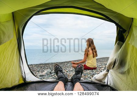 View from inside a tent on the young lady practicing yoga at seashore in summer
