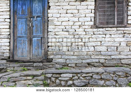 Grunge gray bricks wall with old rough wooden blue door and brown window it is a side view of house.