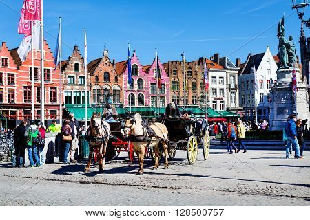 Bruges, Belgium - April 10, 2016: Market place or Grote Markt square with colorful traditional houses, fiaker, people walking in popular belgian destination