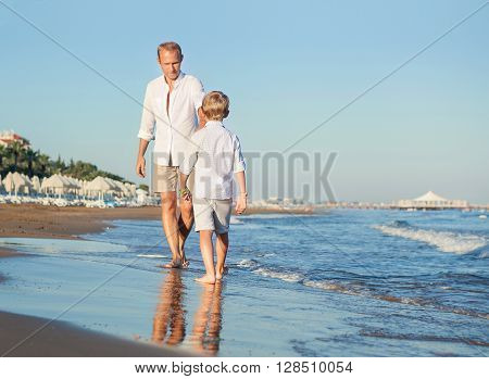 Father with son walking together at the sea surfline