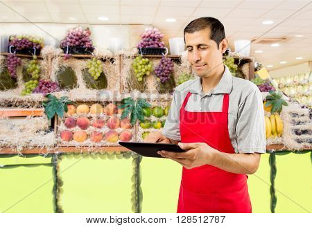 shopman in the greengrocer and fruit shop uses a tablet