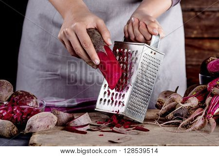 Cook in gray apron is grating a beetroot with vegetable rasper