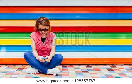 Young woman using a smartphone in front of the colorful walll