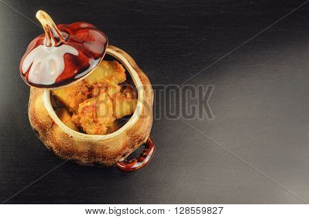 On a black table there is a blue baking dish potato and meat. A dish ready stewed potato with meat