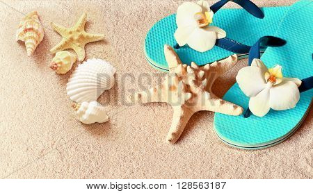 Flip Flops in the sand with starfish and orchid flowers. Summertime on beach concept. Summer beach.