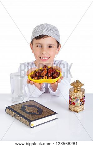 Little Muslim kid smiling while presenting a dish of dates for iftar - breaking fast in Holy Ramadan - showing generous of Ramadan