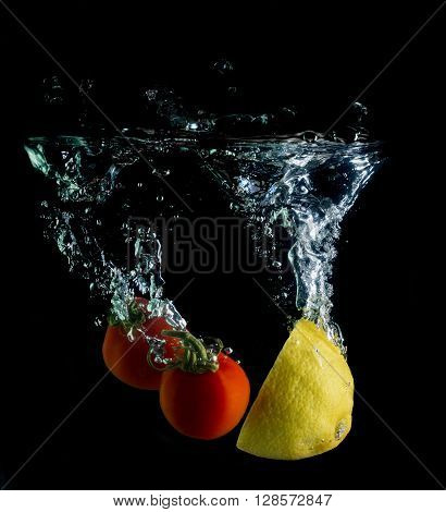 tomatoes and lemon on black background falling into the water