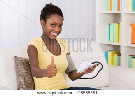 Happy Young African Woman Sitting On Sofa Measuring Blood Pressure At Home