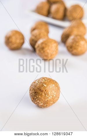 tilgul or til gul laddu, isolated on white background, showing wooden plate full of laddu in background, selective focus