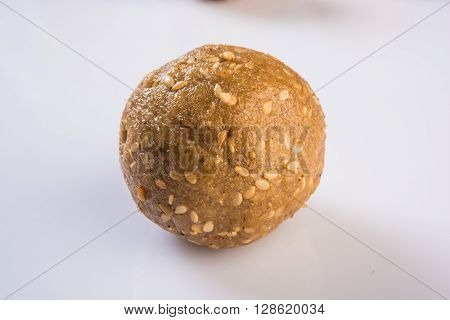 tilgul or til gul laddu, isolated on white background, showing wooden plate full of laddu in background, selective focus