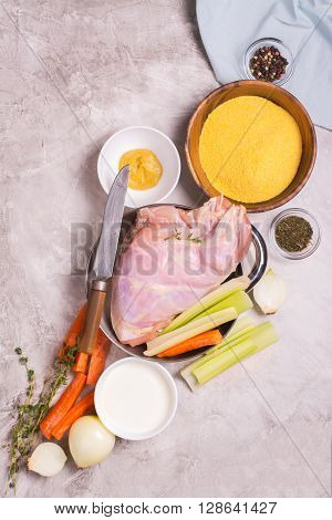 Raw rabbit legs, vegetables, spices and polelnta over stone table. Top view