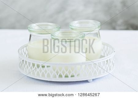Homemade vanilla yogurt in glass jars over white vintage tray