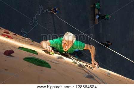 Elderly Male Climber Makes Hard Move on Outdoor Climbing Wall Sport Competitions Very Emotional Face Highlighted with Ray of Illumination