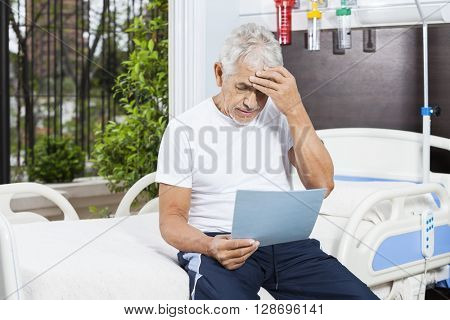 Tensed Senior Man Reading Reports In Rehab Center