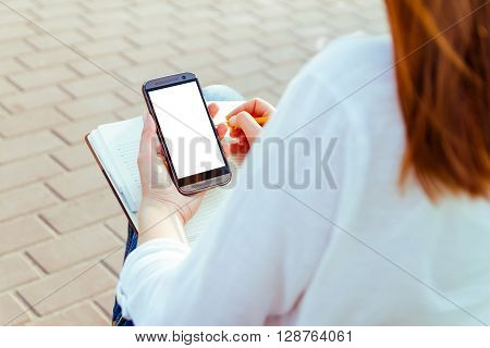 Girl with a phone in her hands, sitting on a bench in the park. Back view. Online shopping concept