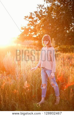 Portrait of young modern girl on the background of nature. Young woman  on a background sunset. Young woman in ripped jeans. in sun glasses