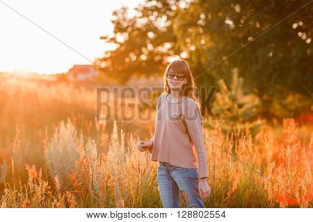 Portrait of young modern girl on the background of nature. Young woman  on a background sunset. Young woman in ripped jeans. in sun glasses