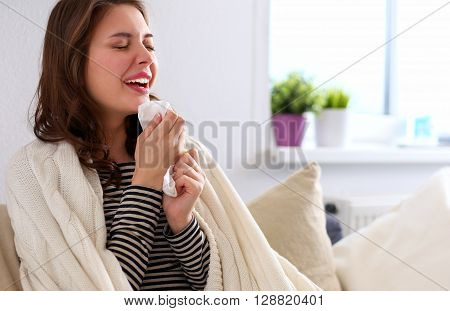 Portrait of a sick woman blowing her nose while sitting on the sofa.