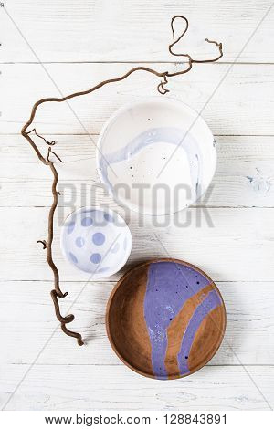 Top view empty creative handmade pottery plates with turquoise pattern on rustic wooden table.  Flat lay set of colorful clay dishes on white wooden background.
