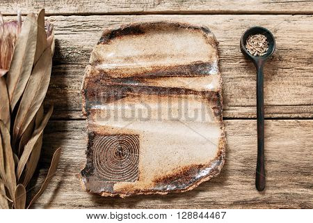 Rustic handmade brown pottery empty big plate on wooden table. Creative brown ceramics with nature pattern. Empty clay dish and wooden spoon on old wooden background with freee space on plate