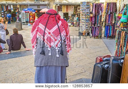 JERUSALEM ISRAEL - FEBRUARY 18 2016: The senior Palestinian in red kufiya walks in Omar Ben el-Hatab street along the souvenir shops on February 18 in Jerusalem.