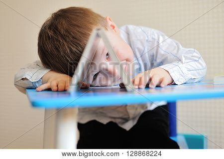 Young schoolboy playing with books and smiling as he sits at his desk in classroom.