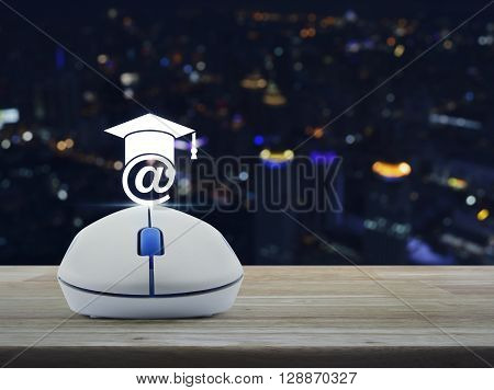 Wireless computer mouse with e-learning icon on wooden table in front of blurred light city tower Study online concept
