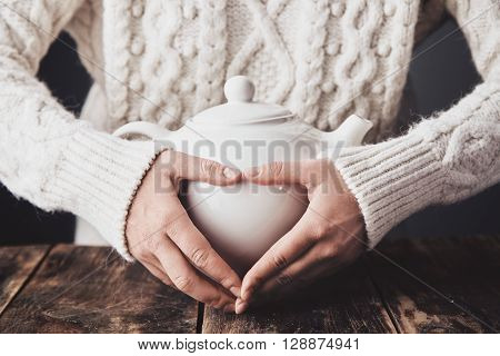 Adult Woman Hands Hug Big Ceramic Teapot With Hot Drink Inside, Making Heart Sign On It. Close Up, W