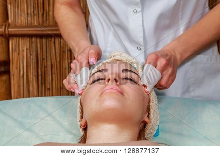 Girl with a beautician at spa salon. Beautician performs cosmetic procedures.applying cosmetic cream. Cosmetology facial beauty - The concept of facial skin care. Article about cosmetology.