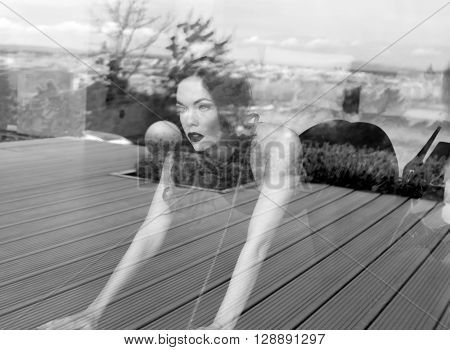Sexy dominatrix in latex catsuit posing behind glass black and white