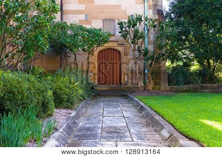 Colorful wooden arch door of sandstone building with stone pavement and green lawn