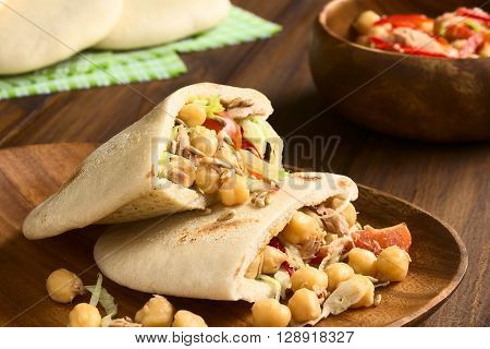 Pita sandwich stuffed with chickpea tuna lettuce pepper cherry tomato roasted sunflower seeds on top photographed with natural light (Selective Focus Focus one third into the stuffing of the upper pita)