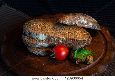 Fresh bread on wooden tablevintage filter Traditional black rye-bread on dark background Red cherry tomatoes with sliced bread vintage still life