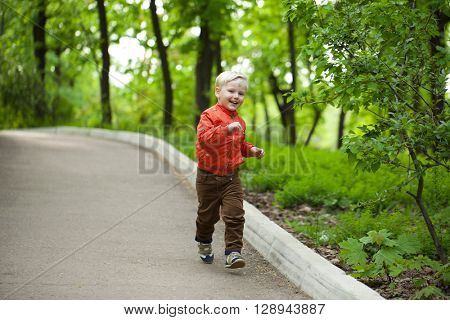 Portrait in full growth, Happy Little boy in orange jacket walking in summer park