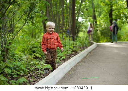 Portrait in full growth, Happy Little boy in orange jacket walking in summer park