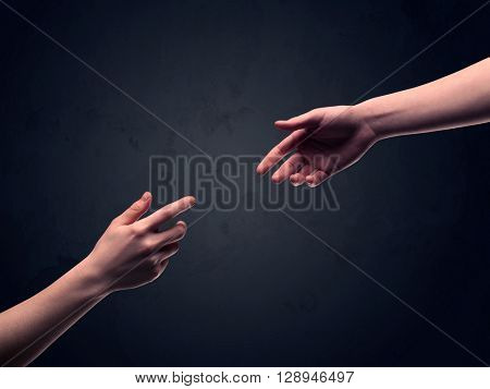 Two male hands reaching out to one another, almost touching, in front of dark clear empty background wall concept