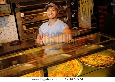 Handsome pizzaiolo standing at kitchen in pizzeria.