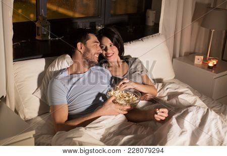 people, family and leisure concept - couple with popcorn watching tv at night at home