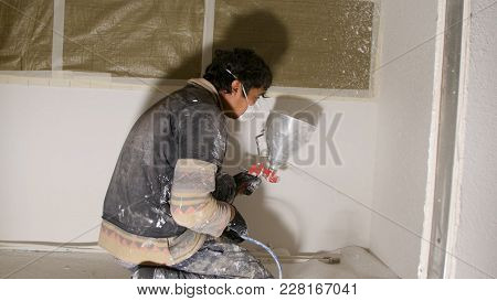 Worker Painting Wall With Spray Gun In White Color. Man Painting A Grey Wall, Renovating Exterior Wa
