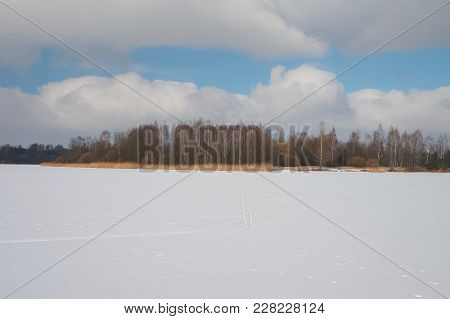 Ice And Snow Covered River, Trees, Rushes, Fallen Fields And Blue Sky With White Clouds. Cold, Snowy