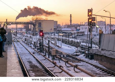 Railway Station In The Snow With Semaphores And Rails In Winter On The Background Of Urban Landscape