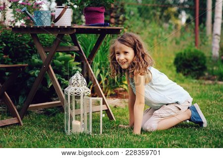 Dreamy Romantic Kid Girl Relaxing In Evening Summer Garden Decorated With Lantern And Candle Holder 